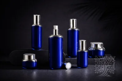 Cobalt blue acrylic skincare bottles and cosmetic jars with silver caps, arranged on dark stone platforms in a sleek set.