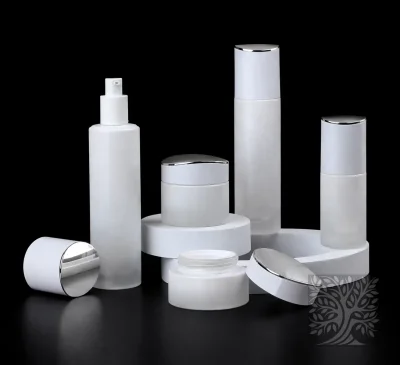 Frosted white skincare bottles and cosmetic jars with chrome lids, arranged on layered white stands with an open jar.