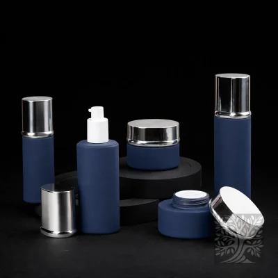 Satin navy blue skincare bottles and jars with silver caps, styled on layered black stands with open jar detail.