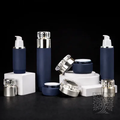 Matte navy blue bottles and cosmetic jars with silver caps, presented on white blocks with spare lids nearby.