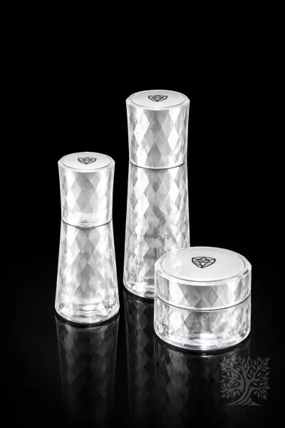 Clear faceted acrylic skincare bottles and cosmetic jar set with prism texture, arranged on black reflective surface.