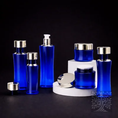 Deep cobalt blue glass bottles and cosmetic jars with silver accents, displayed in a clean elevated product grouping.