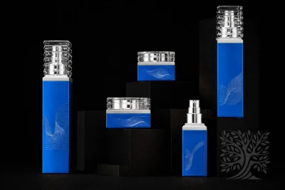 Blue square skincare bottles and cosmetic jars with clear caps and metallic silver accents, arranged on black display blocks.