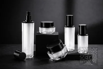 Clear acrylic skincare bottles and cosmetic jars with black caps, displayed on black blocks with open jar detail.