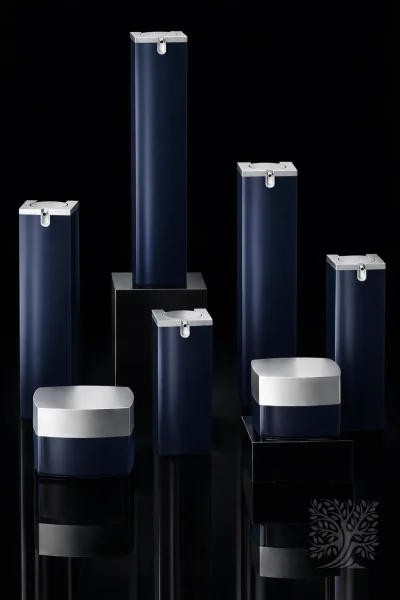 Deep navy glass skincare bottles and cosmetic jars with silver caps, arranged in a refined minimalist display.