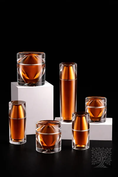 Amber-toned acrylic bottles and jars with clear geometric outer walls, paired in a coordinated skincare packaging lineup.