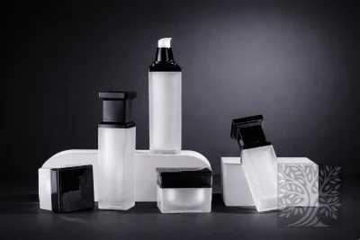 Frosted white acrylic skincare bottles and cosmetic jars with black caps, arranged on stands with open jar and tilted bottle.
