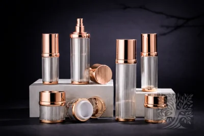 Clear ribbed acrylic bottles and jars with rose gold caps, styled on white blocks with varied heights and open jar detail.