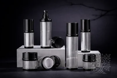 Clear ribbed acrylic skincare bottles and cosmetic jars with black caps, arranged on white platforms in a modern layout.