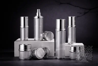 Clear ribbed acrylic skincare bottles and cosmetic jars with silver caps, arranged on white blocks in a refined display.